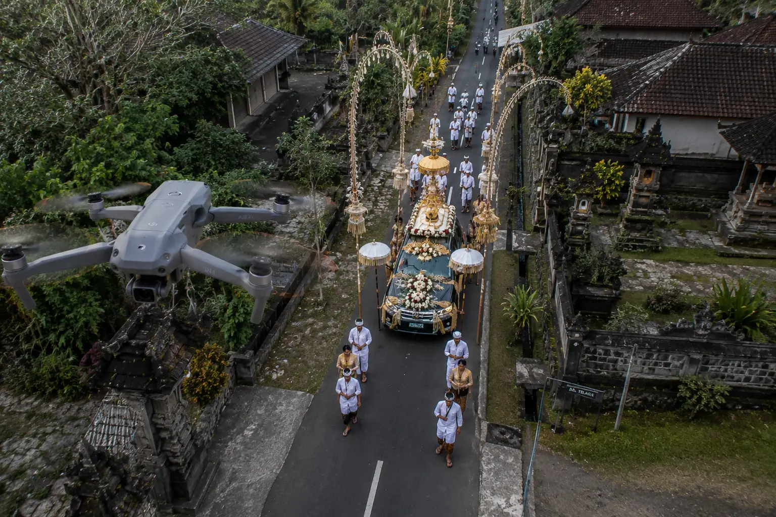 Drone capturing a traditional Balinese wedding procession with decorated wedding vehicle and ceremonial attendants, filmed from above in a Bali village using professional drone videography.